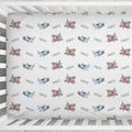 A white crib bedding set featuring a repeating pattern of vintage airplanes in gray, pink, and brown, with the name 'PARKER' printed in black between each aircraft.