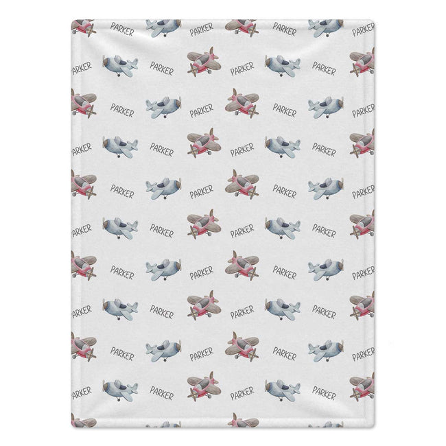 Personalized Airplane Baby Blanket. Watercolor airplanes surround a custom name in soft blue, grey, and pink tones on a white background.