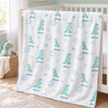 A personalized baby blanket with a green dinosaur and blue cloud pattern, printed with the name 'Mia' multiple times, draped over a white crib in a nursery setting.