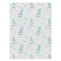 A personalized baby blanket featuring a repeating pattern of light blue watercolor dinosaurs, clouds, stars, and the name 'Alana' printed in blue script.