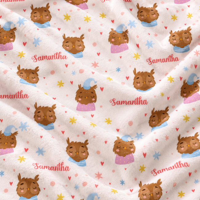 A close-up of a soft fleece blanket with a repeating pattern of cartoon owl wearing blue hats and pink dresses, scattered yellow and blue stars, small red hearts, and the name 'Samantha' printed in red script.