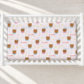 A baby crib mattress fitted sheet with a repeating pattern of cartoon owls, stars, and the name 'Samantha' in pink, shown inside a white wooden crib.