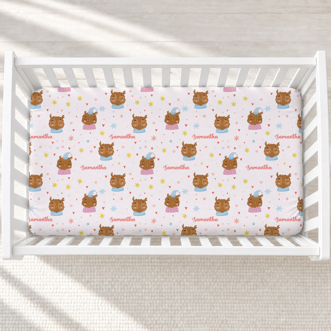 A baby crib mattress fitted sheet with a repeating pattern of cartoon owls, stars, and the name 'Samantha' in pink, shown inside a white wooden crib.