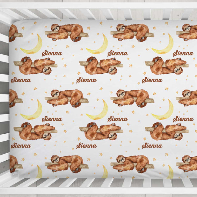 A fitted crib sheet with a repeating pattern of brown sloths sleeping on branches next to yellow crescent moons and small gold stars on a white background. The name 'Sienna' is printed in brown script below each sloth.