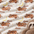 A close-up of a plush white fabric printed with watercolor sloths on branches, yellow crescent moons, small gold stars, and the name 'Sienna' repeated in brown script. A stuffed sloth is partially visible at the lower right edge.