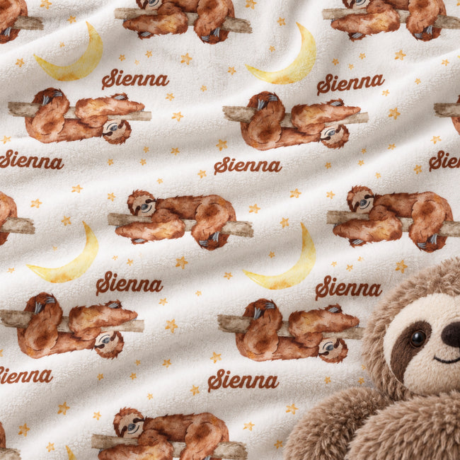 A close-up of a plush white fabric printed with watercolor sloths on branches, yellow crescent moons, small gold stars, and the name 'Sienna' repeated in brown script. A stuffed sloth is partially visible at the lower right edge.