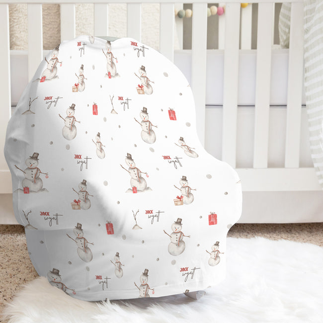 A baby car seat cover with a winter snowman pattern, displayed on a white baby crib in a nursery setting.