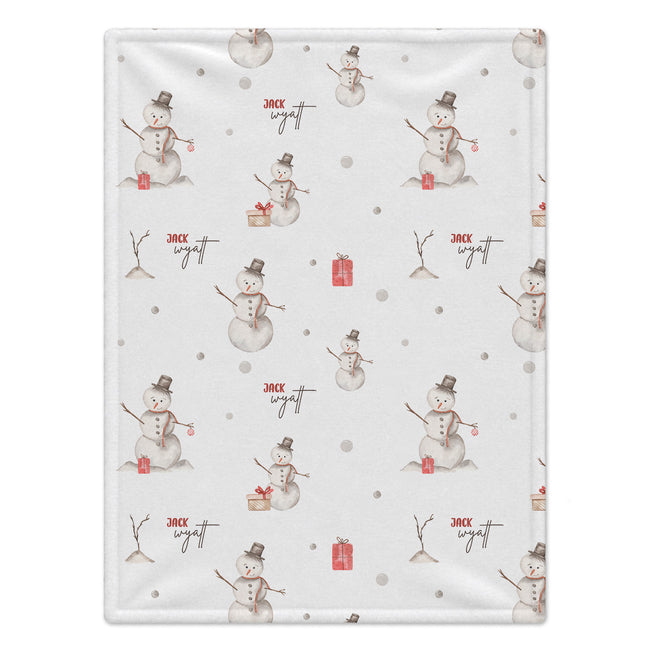 A personalized baby blanket with a white background featuring a repeating pattern of snowmen, small red gift boxes, and the name 'Jack Wyatt' in red script.