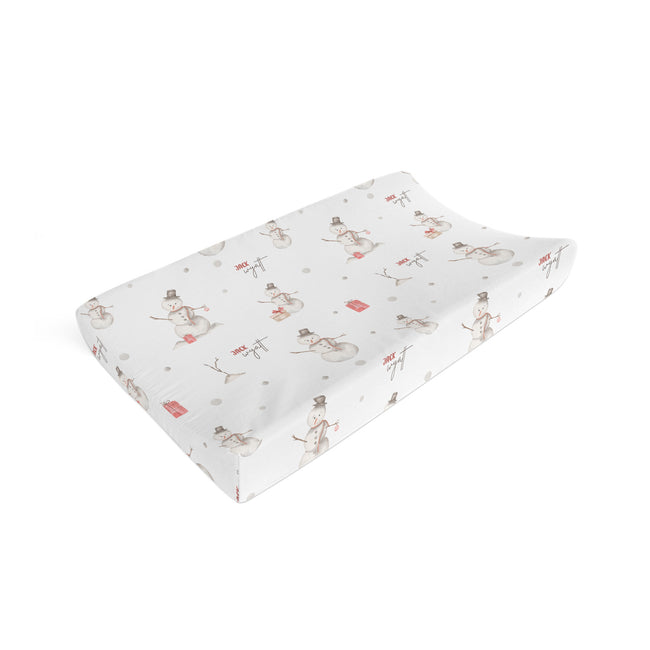 A contoured baby changing pad cover with a white background and a repeating pattern of snowmen in brown and red, shown on a clean white background.