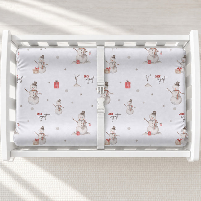 A white changing table with a personalized changing pad cover featuring white background and a winter snowman pattern.