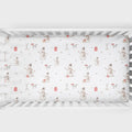 A fitted crib sheet with a winter holiday snowman pattern, shown inside a white wooden baby crib.