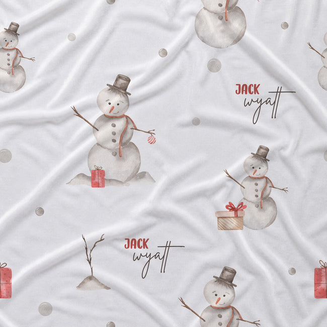 White fabric with a repeating pattern of watercolor snowmen, small red gift boxes, gray dots, and the personalized text 'JACK wyatt' in red and black script.