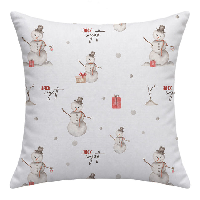 A square white throw pillow featuring a repeating pattern of watercolor snowmen in gray and brown, small red gift boxes, and the name 'Jack Wyatt' in a cursive font.