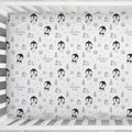 A crib bumper or fitted sheet with a repeating penguin and forest pattern on a white background, shown inside a white wooden crib. The pattern includes penguins, trees, mountains, and the text 'clara mae'.