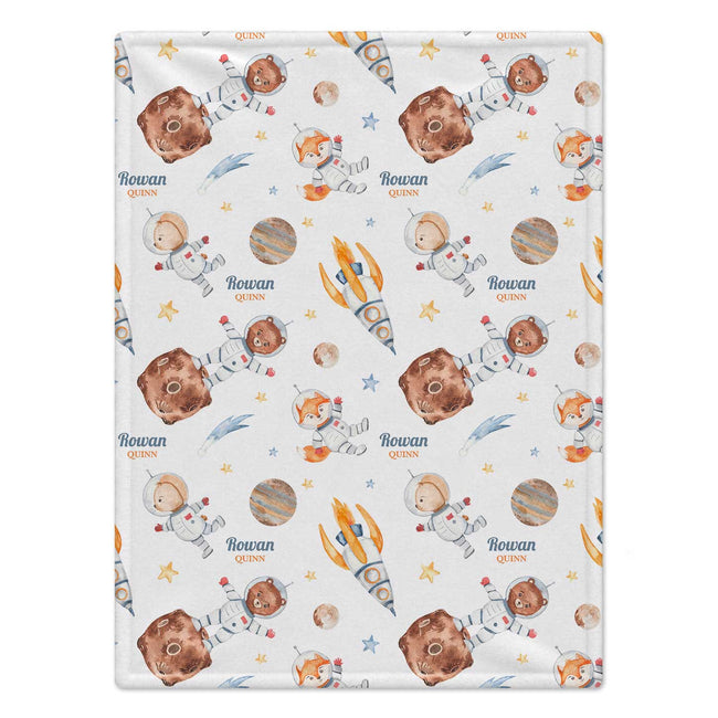 A personalized blanket with a space-themed print featuring cartoon astronauts, planets, stars, and the name 'Rowan QUINN' repeated on a white background.