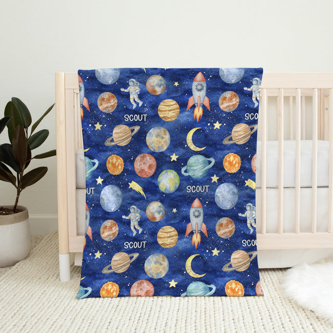 Full view of the Space Explorers personalized blanket with white Scout lettering and colorful watercolor space illustrations on a navy starry background.