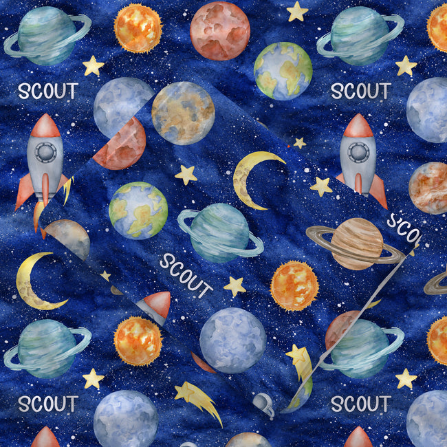 Close-up of the folded Space Explorers swaddle blanket showing white Scout lettering, colorful watercolor planets, and rockets on navy.
