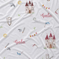 White fabric with a repeating pattern of watercolor-style castles, flags, swords, shields, clouds, and the word 'Gala' in pink script.