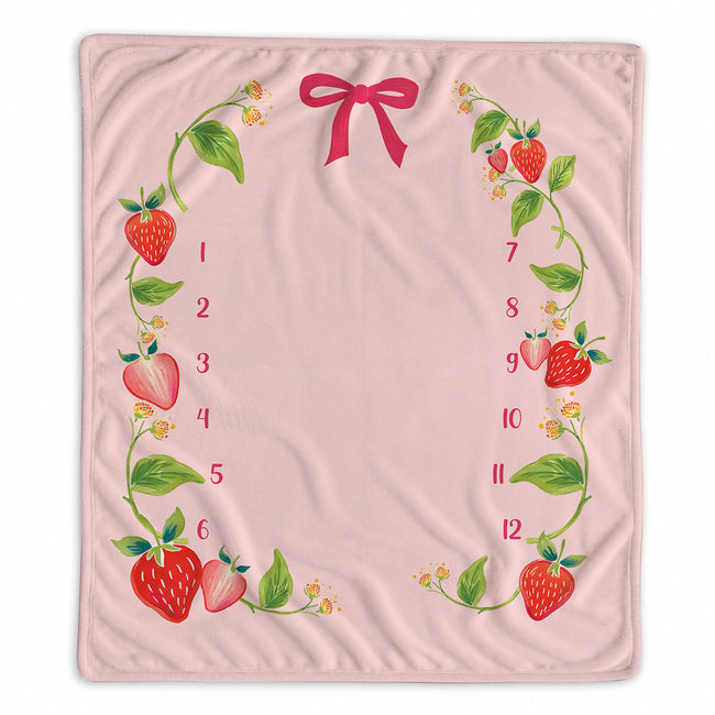 A baby milestone blanket featuring a decorative border of illustrated strawberries, green leaves, small yellow flowers, and red bow accents, with red numbers 1 through 12 arranged along the left and right sides.