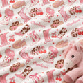 A close-up of a pink and brown western-themed fabric print featuring cowboy boots, hats, cherries, hearts, and the name 'Marlowe' in script, with a plush pink horse toy partially visible in the lower right corner.