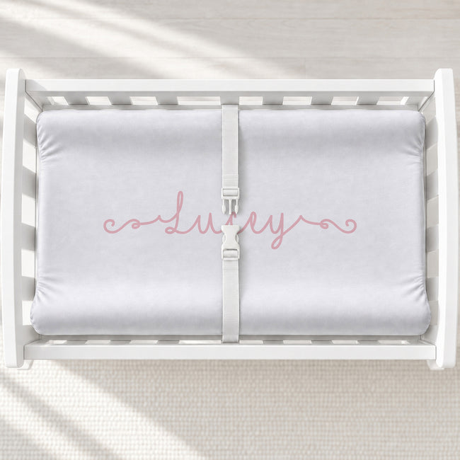 A white changing table with a personalized changing pad cover featuring a personalization with a swirly font with the name Lucey centered on the cover.