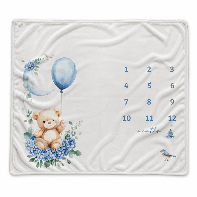 Baby boy milestone blanket featuring a teddy bear, blue balloon, floral moon, and monthly number grid.