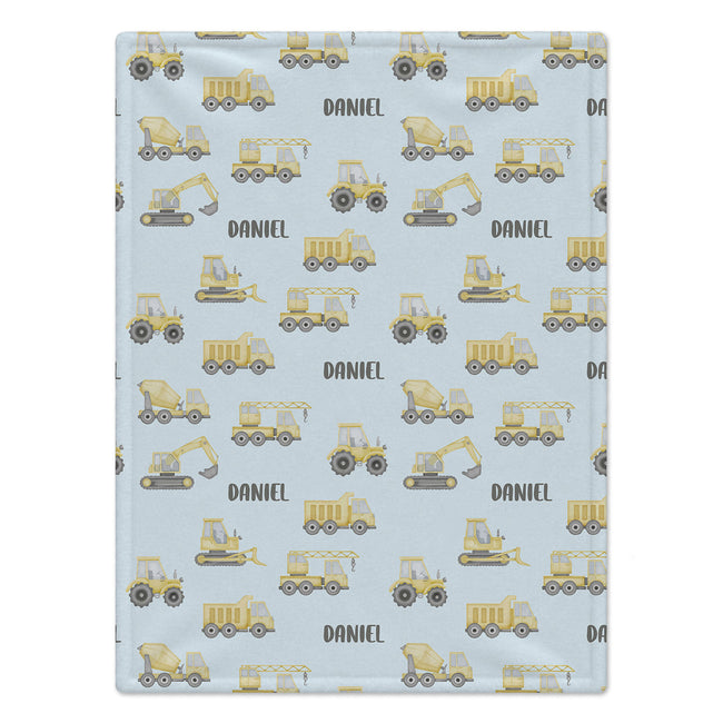 A personalized baby blanket with a light blue background, featuring a repeating pattern of yellow construction vehicles and the name 'DANIEL' printed in black.