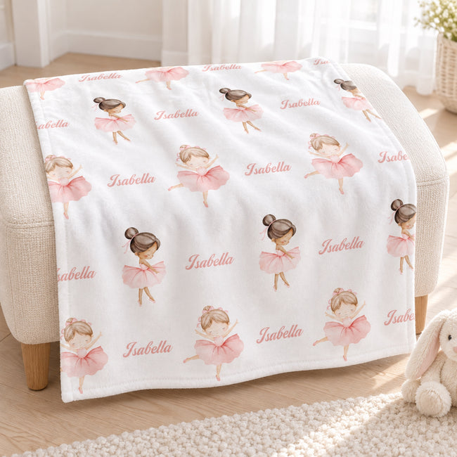 A white blanket with a repeating pattern of ballerina illustrations and the name 'Isabella' is draped over a cream-colored armchair in a bright, softly lit room.