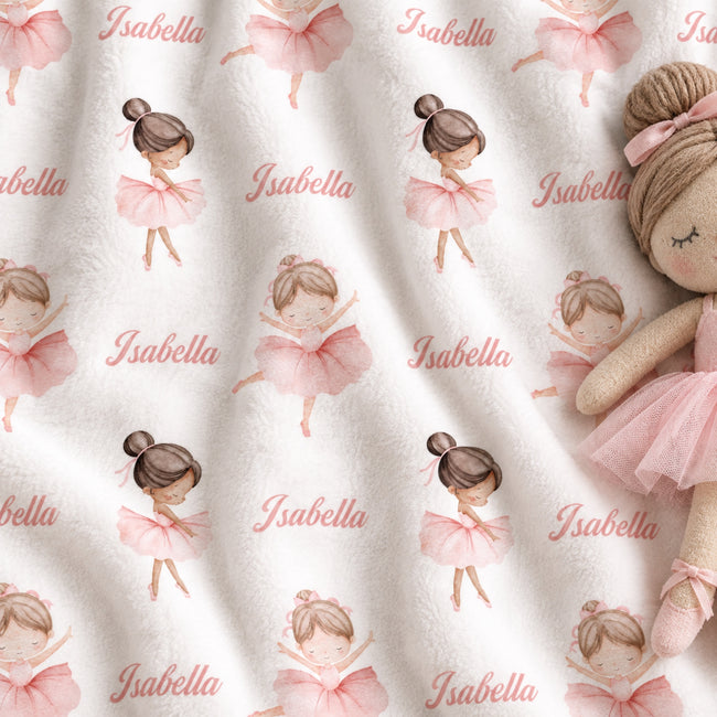 A close-up of a white plush blanket or fabric printed with repeated ballerina illustrations, the name 'Isabella' in pink script, and a soft doll partially visible on the right side.