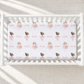 A white crib fitted with a custom printed sheet featuring a repeating pattern of ballerina illustrations and the name 'Isabella' in pink script.