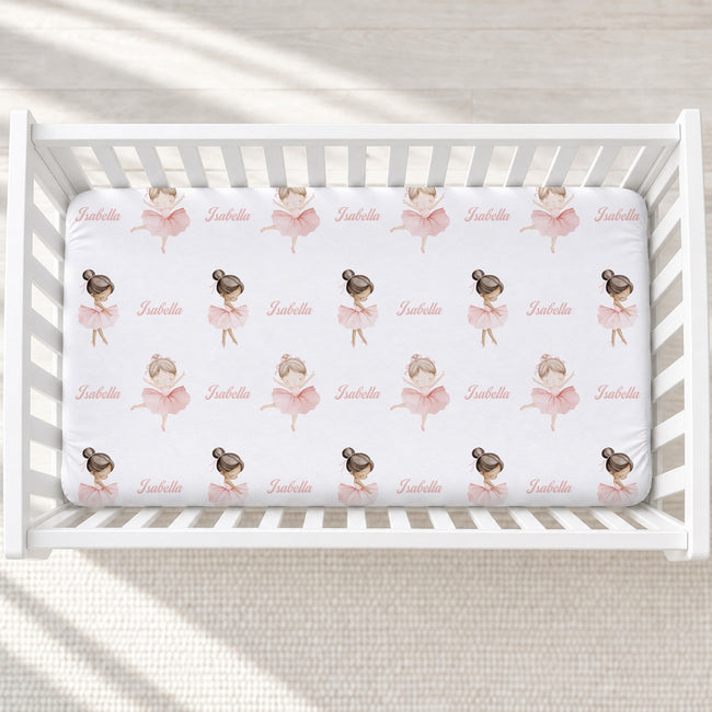 A white crib fitted with a custom printed sheet featuring a repeating pattern of ballerina illustrations and the name 'Isabella' in pink script.