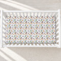 A fitted crib mattress with a colorful tropical pirate-themed print, shown inside a white wooden baby crib on a light textured floor.
