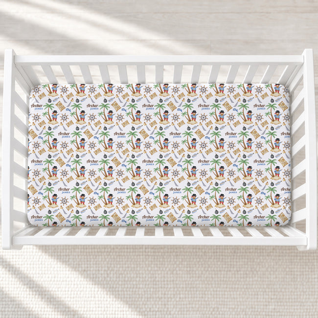 A fitted crib mattress with a colorful tropical pirate-themed print, shown inside a white wooden baby crib on a light textured floor.
