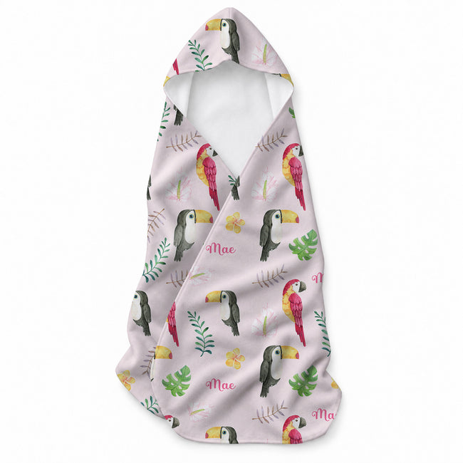Pale pink hooded towel featuring red and yellow parrots, toucans, tropical leaves, flowers, butterflies, and the name Mae.