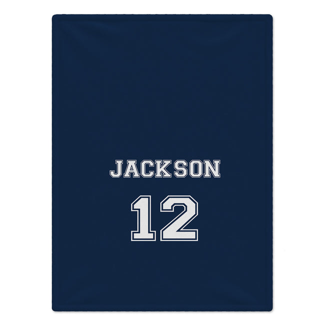 A navy blue blanket featuring the name 'JACKSON' and number '12' printed in white varsity-style lettering with a thin white outline.