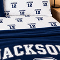 A personalized bedding set featuring a navy blue and white comforter and matching pillowcases printed with the name 'Jackson' and number '12' in a sports jersey style.