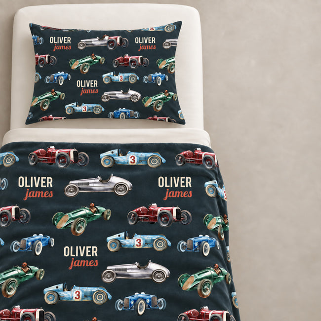 Custom racing-themed bedding set featuring a duvet cover and matching pillowcase with a dark navy background, printed with vintage race cars in red, blue, green, and silver, and personalized with the name 'Oliver James'.