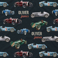 A dark navy fabric featuring a repeating pattern of vintage racing cars in blue, green, red, and silver, interspersed with the personalized text 'OLIVER james' in cream and coral.