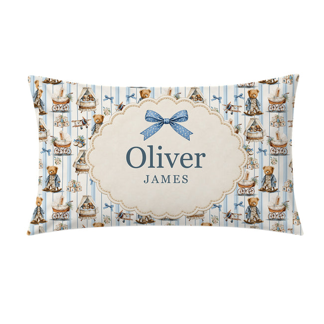 A personalized pillowcase featuring a blue and cream teddy bear pattern, with a central cream label containing the names 'Oliver' and 'JAMES' and a blue bow illustration.