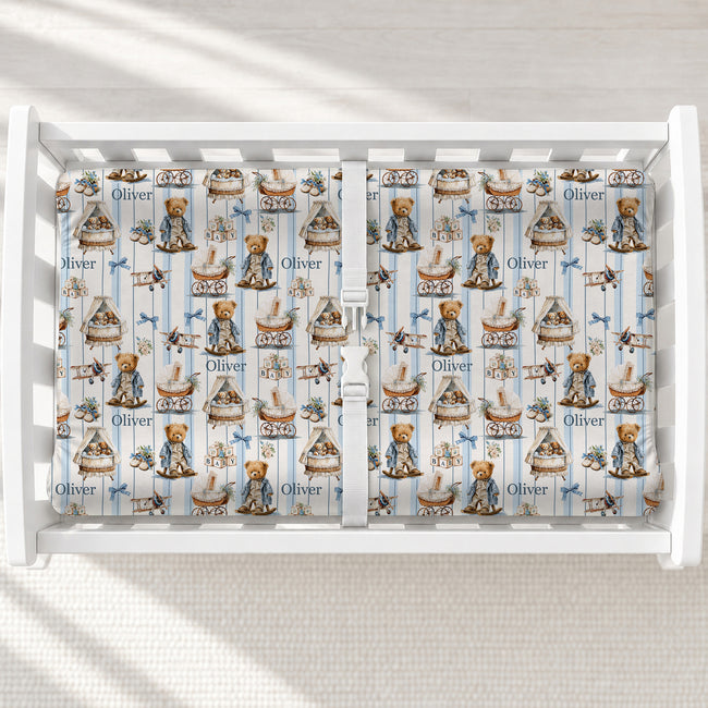 A white changing table with a personalized changing pad cover featuring a repeating pattern of teddy bears in strollers and carriages, blue stripes, and the name 'Oliver'.