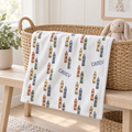A white baby blanket with a colorful crayon pattern and the name 'CASEY' printed on it, draped over a woven wicker basket in a bright nursery setting.