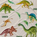 A close-up of a fabric surface printed with multiple colorful dinosaur illustrations and the word 'CAIDEN' repeated, showing a green Stegosaurus, yellow Triceratops, blue T-rex, brown Pteranodon, and green Brachiosaurus.