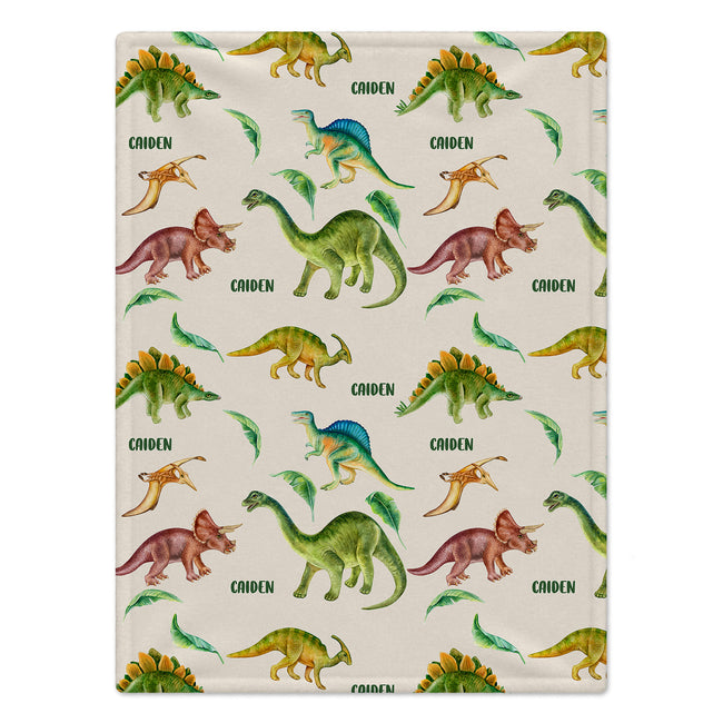 A rectangular blanket with a repeating dinosaur pattern on a cream background. The print features various colorful dinosaurs in green, yellow, blue, and brown, with the name 'CAIDEN' repeated in green text.
