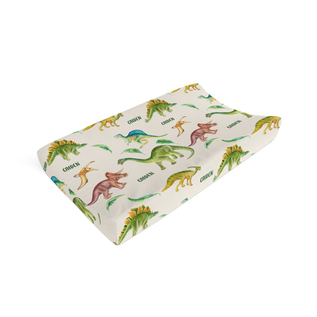 A personalized baby changing pad with a dinosaur print, shown at an angle on a plain white background.