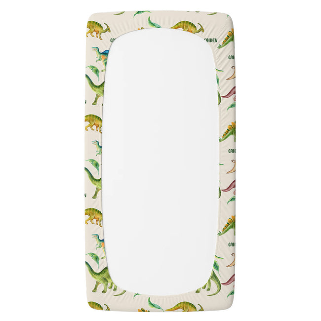 A personalized twin fitted sheet with an elasticized corner border, featuring a colorful dinosaur pattern on an off-white background.