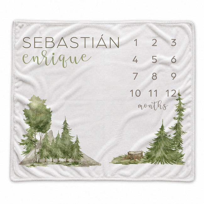 Personalized watercolor forest baby milestone blanket with evergreen trees, mountains, custom name, and months 1–12
