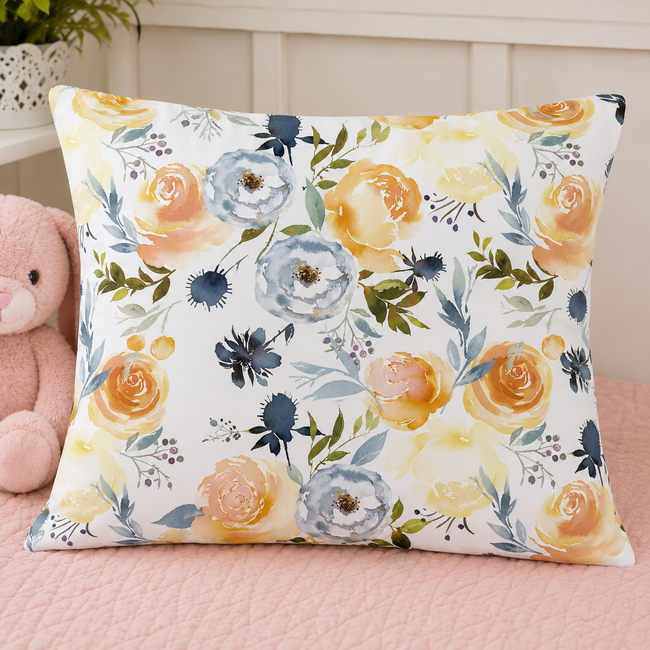 A toddler pillowcase with a watercolor floral pattern in yellow, blue, and green on a white background, resting on a pink bed next to a plush teddy bear.