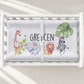 A personalized white changing pad featuring a watercolor giraffe (off-screen), elephant, lion, zebra and plants with the name "GREYCEN" in black, capitalized letters.