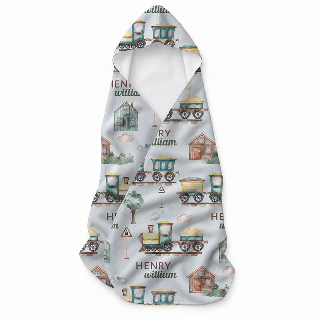 Pale blue hooded towel with watercolor-style trains, railway tracks, houses, trees, clouds, and the name Henry William.