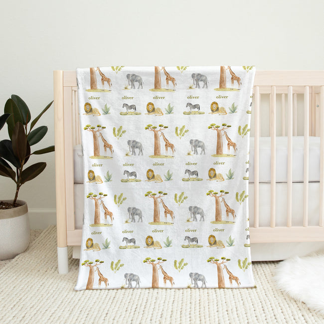 Wildwood Safari personalized baby blanket featuring elephants, giraffes, lions, and zebras, draped over a natural wood crib.